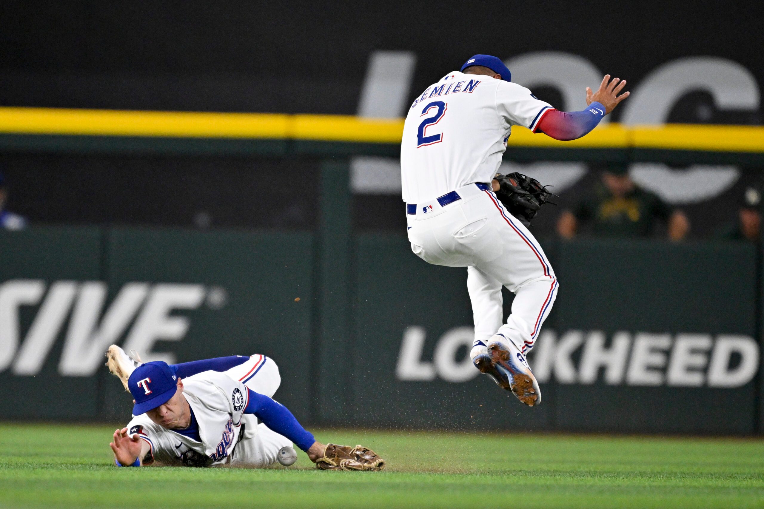Jul 23, 2025; Arlington, Texas, USA; Texas Rangers center fielder Michael Helman (24) dives but cannot catch a ball hit by Athletics left fielder Miguel Andujar (not pictured) as second baseman Marcus Semien (2) attempts to get out of way during the sixth inning at Globe Life Field. Mandatory Credit: Jerome Miron-Imagn Images