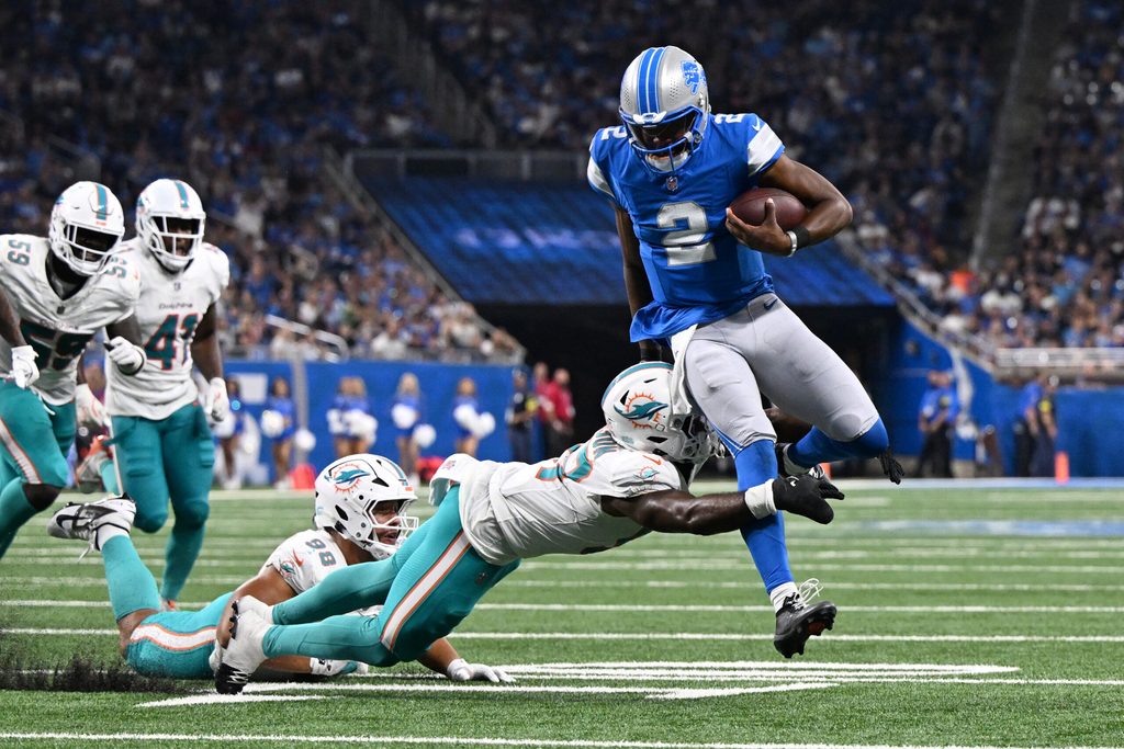 Aug 16, 2025; Detroit, Michigan, USA; Detroit Lions quarterback Hendon Hooker (2) scrambles away from Miami Dolphins linebacker Dequan Jackson (57) to score a touchdown that was nullified by an offensive penalty in the third quarter at Ford Field. Mandatory Credit: Lon Horwedel-Imagn Images