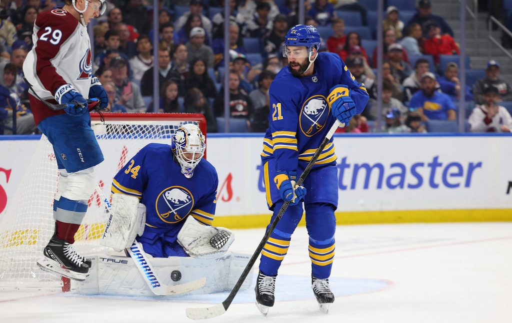 Oct 13, 2025; Buffalo, New York, USA; Buffalo Sabres goaltender Alex Lyon (34) makes a save as Colorado Avalanche center Nathan MacKinnon (29) and Buffalo Sabres defenseman Conor Timmins (21) wait for a rebound during the third period at KeyBank Center. Mandatory Credit: Timothy T. Ludwig-Imagn Images