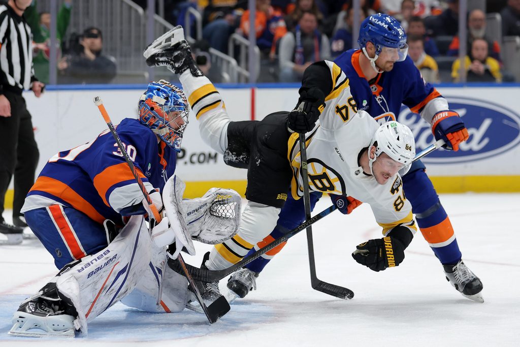 Nov 4, 2025; Elmont, New York, USA; Boston Bruins left wing Tanner Jeannot (84) is upended by New York Islanders defenseman Scott Mayfield (24) in front of Islanders goaltender Ilya Sorokin (30) during the third period at UBS Arena. Mandatory Credit: Brad Penner-Imagn Images