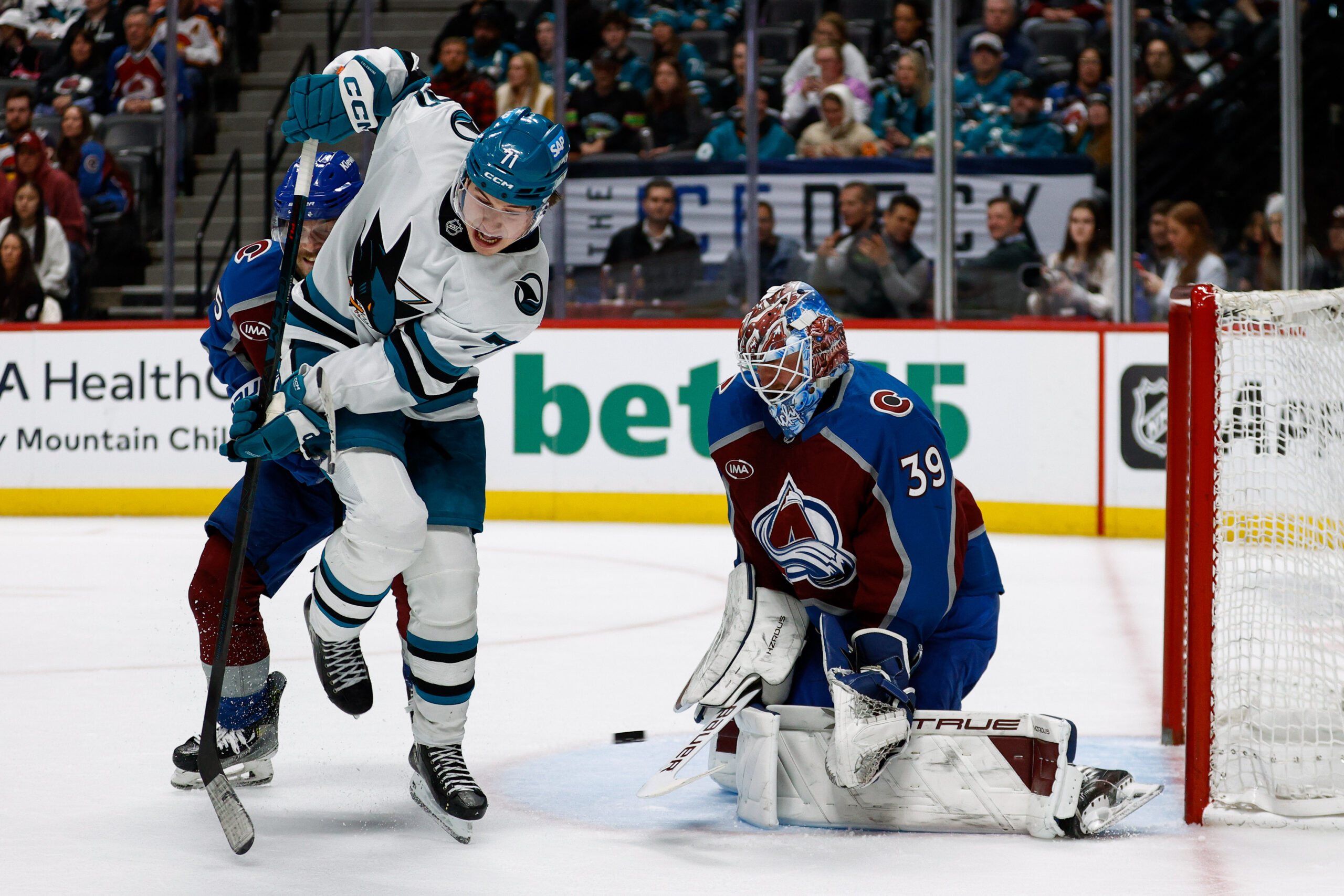 Mar 6, 2025; Denver, Colorado, USA; San Jose Sharks center Macklin Celebrini (71) attempts to deflect the puck against Colorado Avalanche goaltender Mackenzie Blackwood (39) as defenseman Ryan Lindgren (55) defends in the third period at Ball Arena. Mandatory Credit: Isaiah J. Downing-Imagn Images